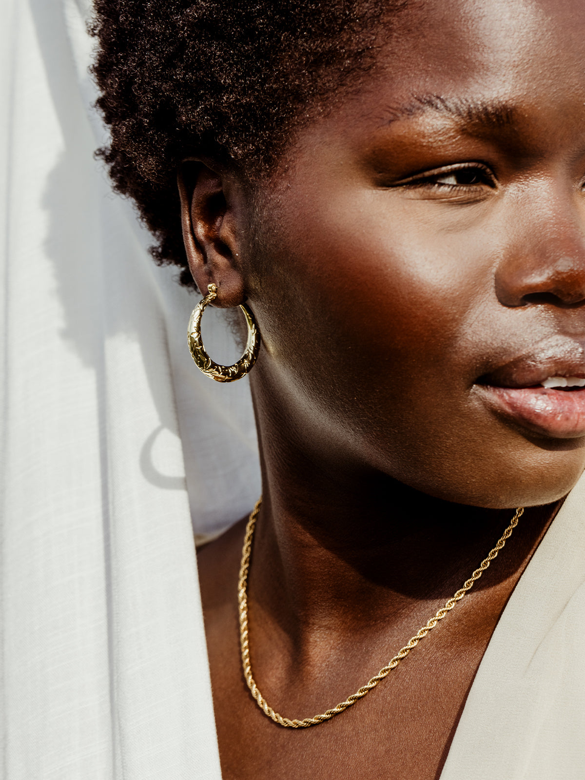 Female African model on white background wearing gold leaf of awareness hoop earrings.