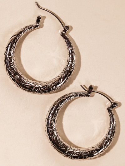 Silver hoop earrings with engraved leaf design on cream background. 