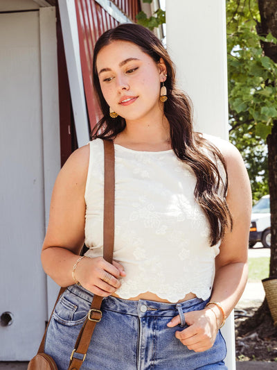 Woman wearing handcrafted white leather and brass fan-shaped earrings paired with a casual outfit, outdoors in a sunny setting.