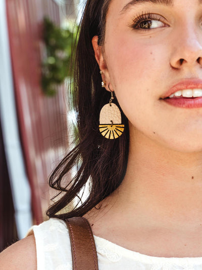 Woman wearing handcrafted blush leather and brass fan-shaped earrings paired with a casual outfit, outdoors in a sunny setting.