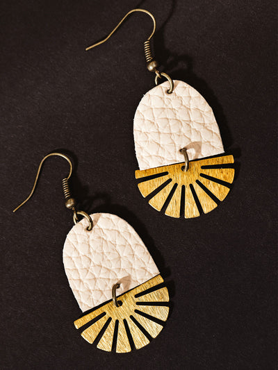 Close-up of handcrafted earrings featuring quilted blush pink leather and brass fan-shaped accents, displayed on a dark background.