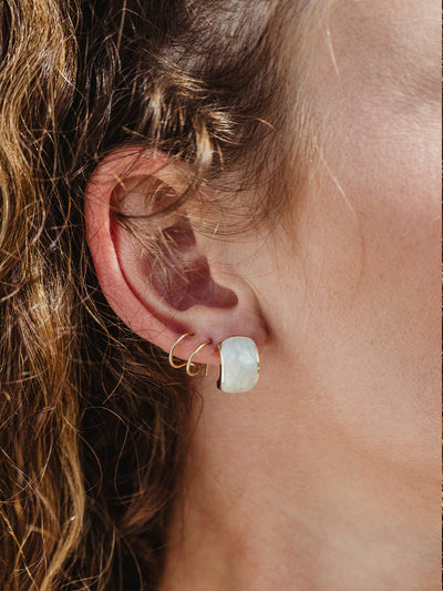 White female model with silver journey of hope huggie earring in ear and an additional earring.