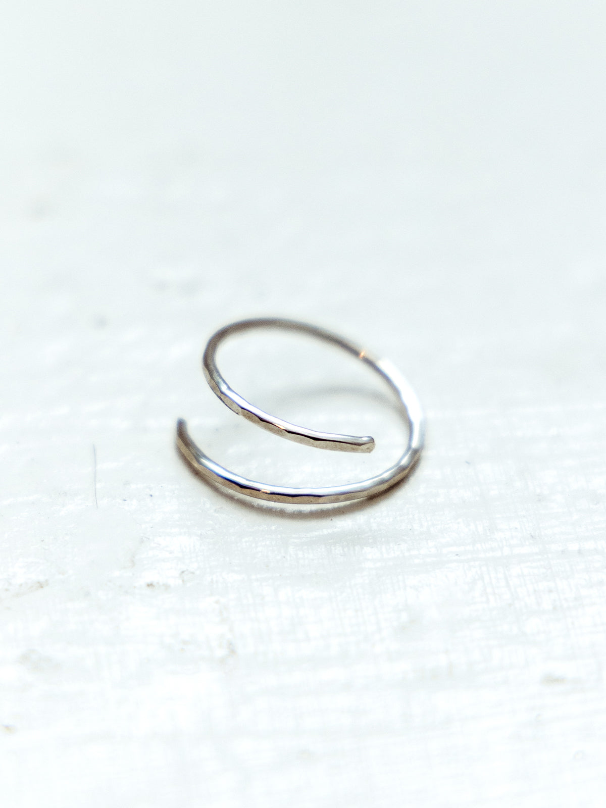 Hammered minimalistic silver wrap ring on white textured surface.