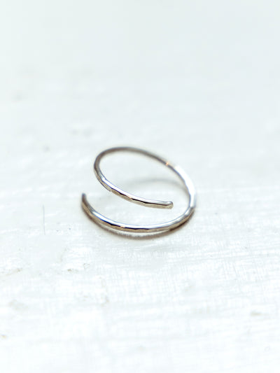 Hammered minimalistic silver wrap ring on white textured surface.