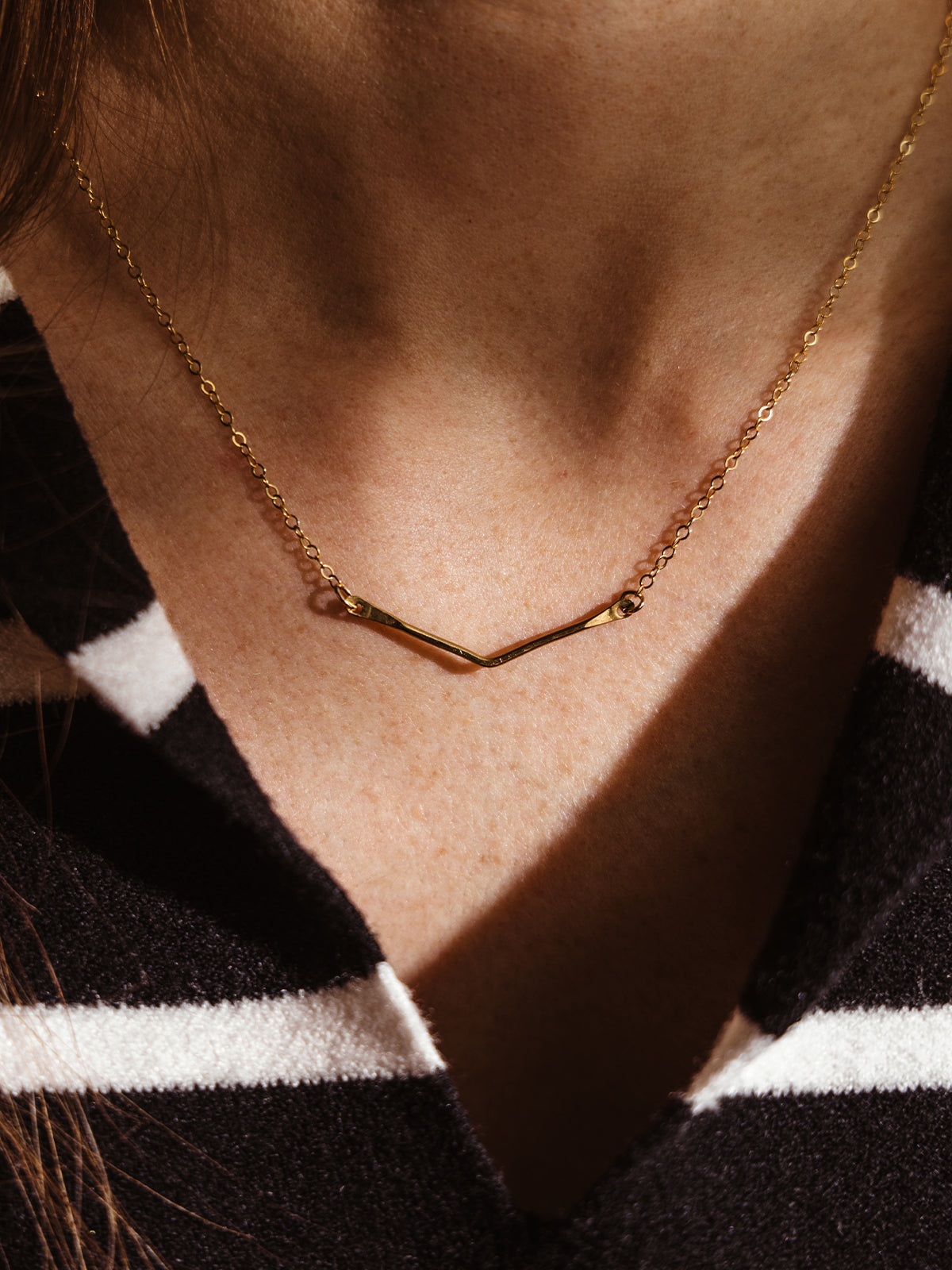 Minimalist gold V-shaped pendant necklace resting on a woman's collarbone. A delicate and modern jewelry piece for everyday wear.