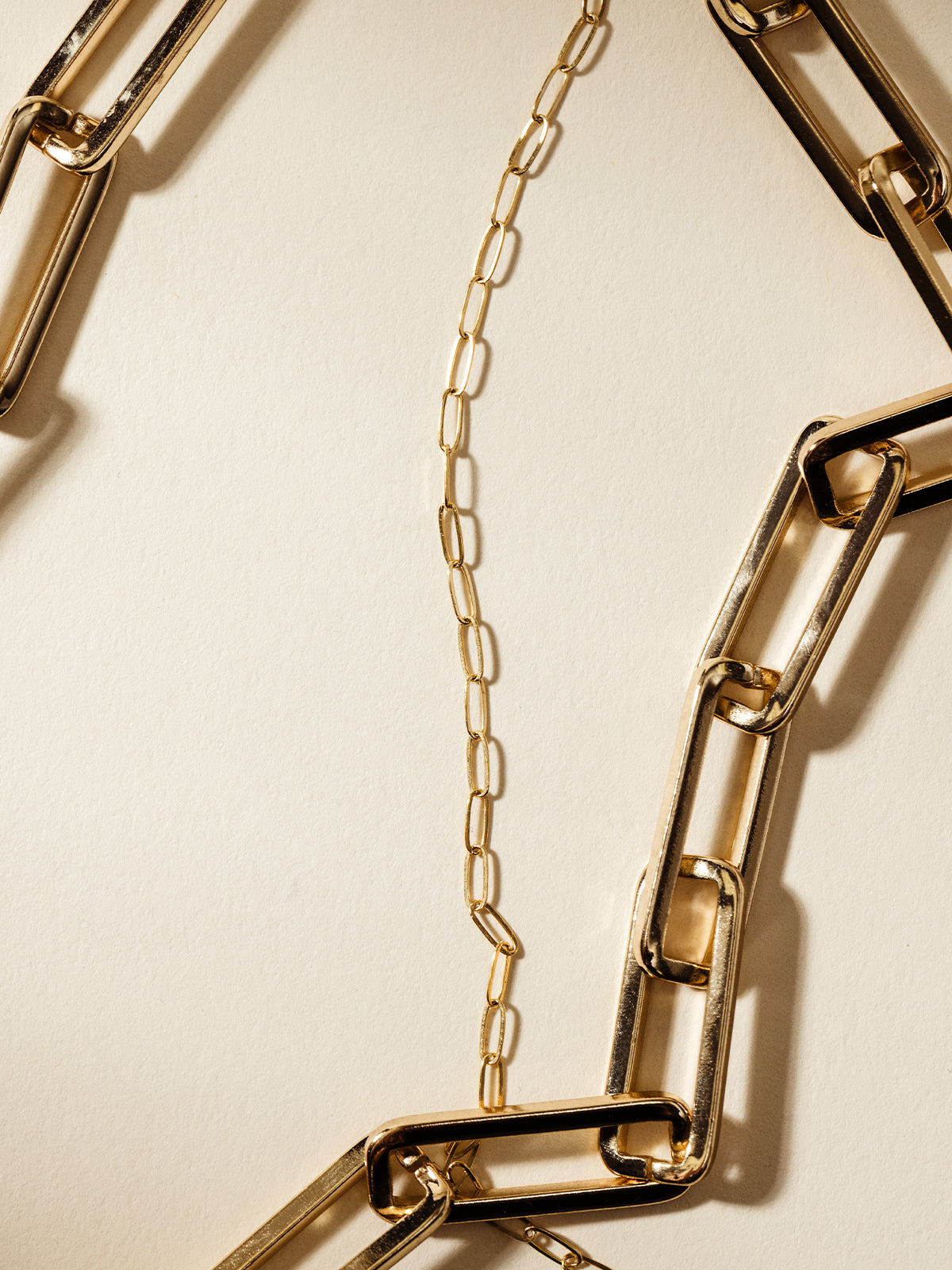 A detailed shot of a gold paperclip chain necklace next to a statement chunky gold link necklace, emphasizing the contrast between modern minimalism and bold style.