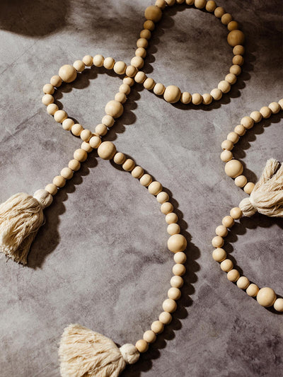 Handmade wooden bead garland with natural fiber tassels arranged on a grey stone surface, casting soft shadows.