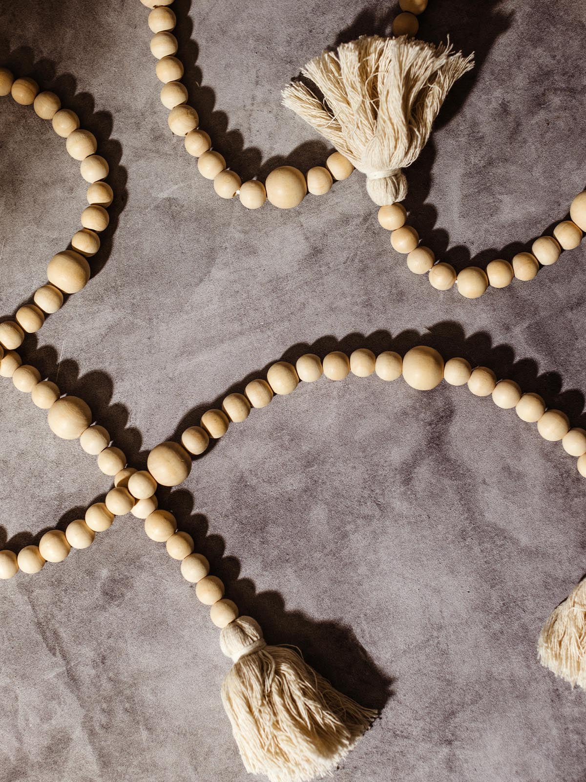 Close-up of a handmade wooden bead garland with large natural fiber tassels, laid out on a grey stone background, highlighting the texture and craftsmanship.