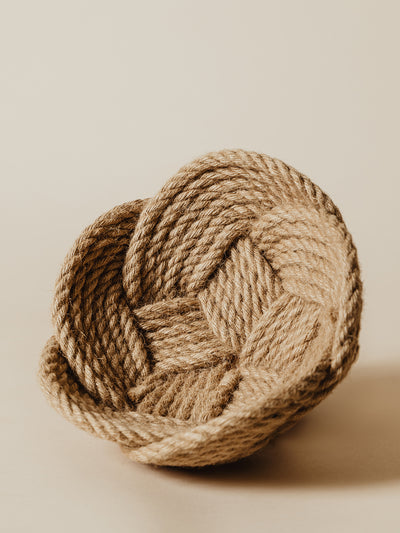 Detailed view of a handwoven rope basket, focusing on its thick, braided edge and natural texture. The basket is placed on a soft, neutral background, emphasizing its minimalist and rustic design.