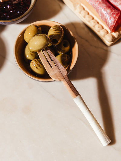 Appetizer serving fork on white counter with charcuterie foods and spreads.