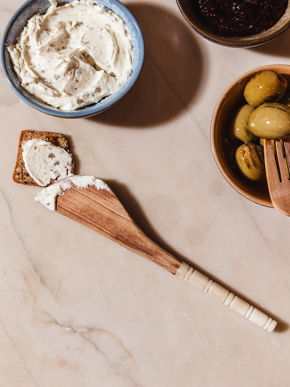 Appetizer serving spreader on white counter with charcuterie foods and spreads.