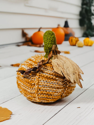 Crocheted pumpkin of front porch with pumpkins and leaves in the background. 
