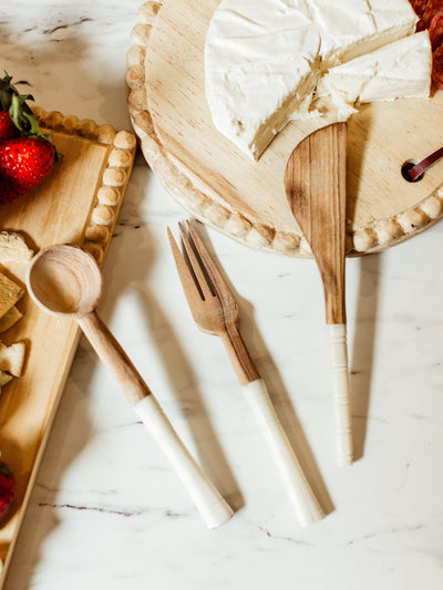 Wood and horn serving utensils on white countertop with serving boards with barriers and cheeses.