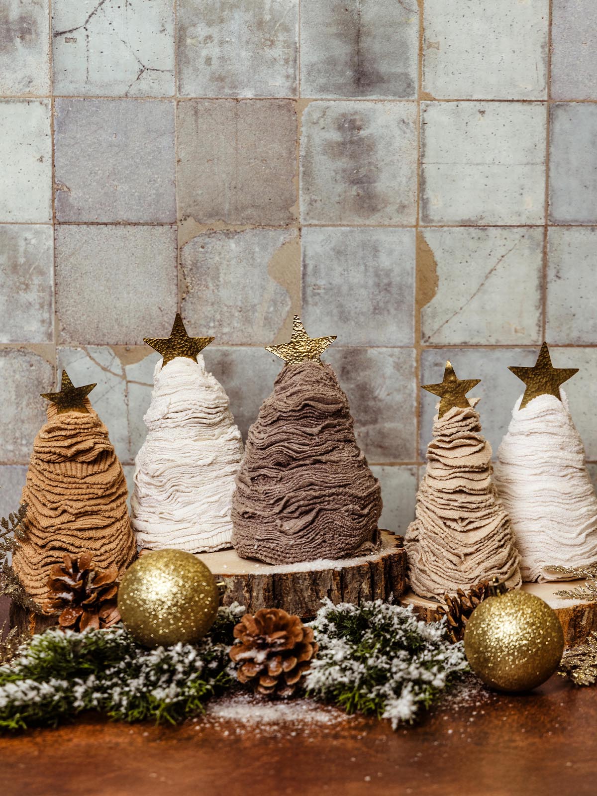 Set of handmade fabric Christmas trees in shades of brown, white, and beige, topped with gold stars, decorated with pinecones and glitter ornaments. Sustainable holiday decor from Joffa.