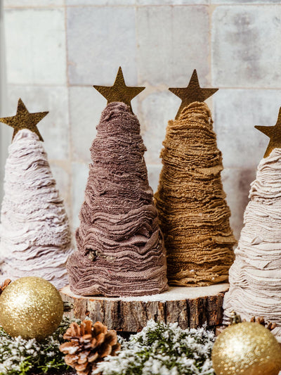 Handcrafted fabric Christmas trees in neutral tones with gold star toppers, surrounded by pinecones and glittering gold ornaments. Ethically made holiday decor from Joffa.