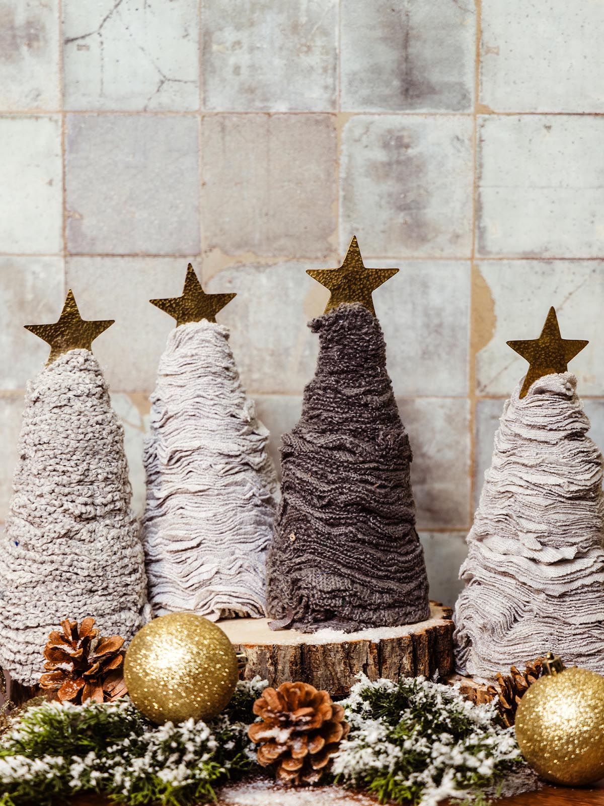 Set of handmade fabric Christmas trees in shades of brown, white, and beige, topped with gold stars, decorated with pinecones and glitter ornaments. Sustainable holiday decor from Joffa.