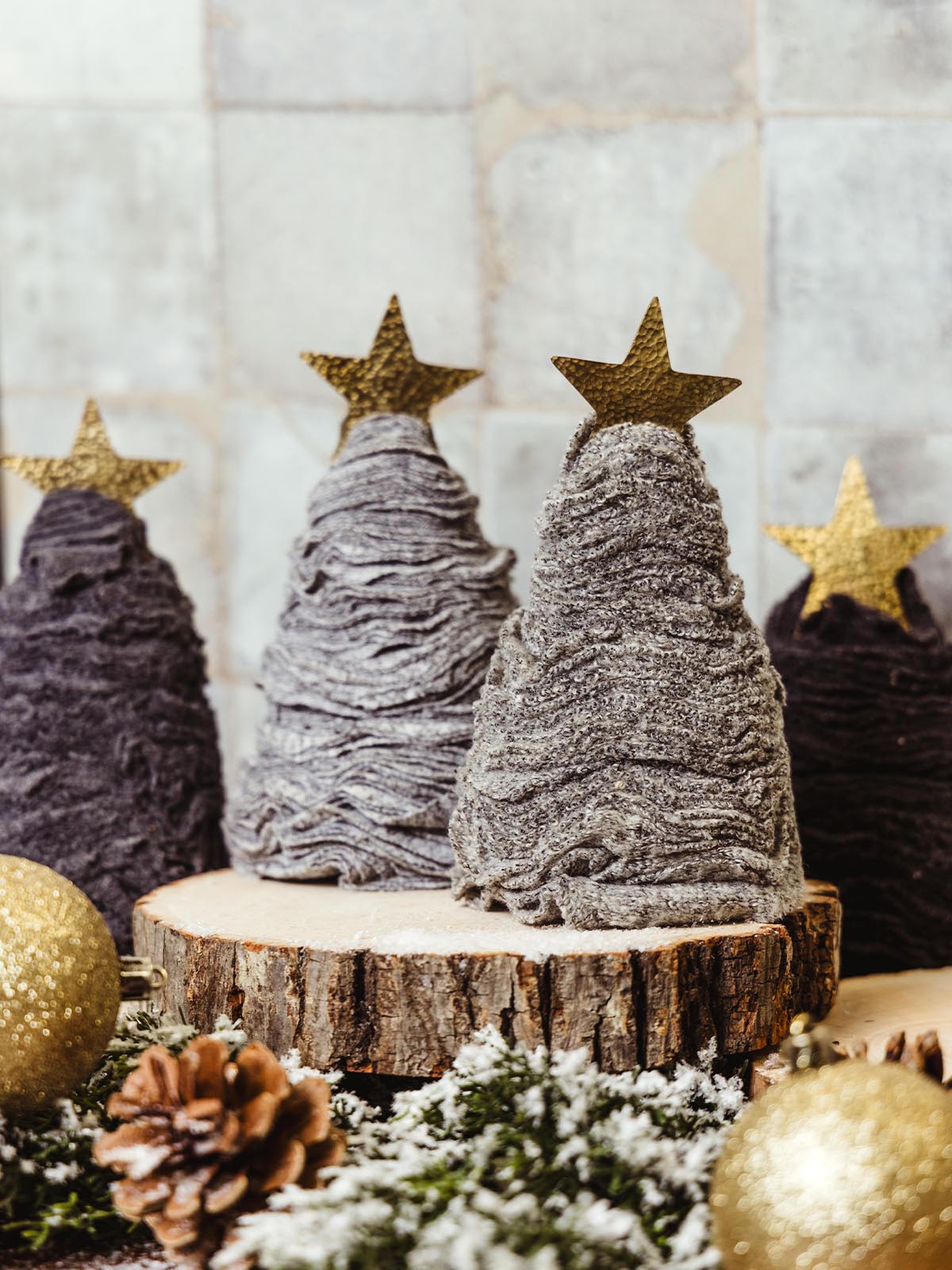 Rustic fabric Christmas trees in neutral tones, decorated with gold stars, pinecones, and glittering ornaments on a snowy holiday display. Ethically sourced holiday decor from Joffa.