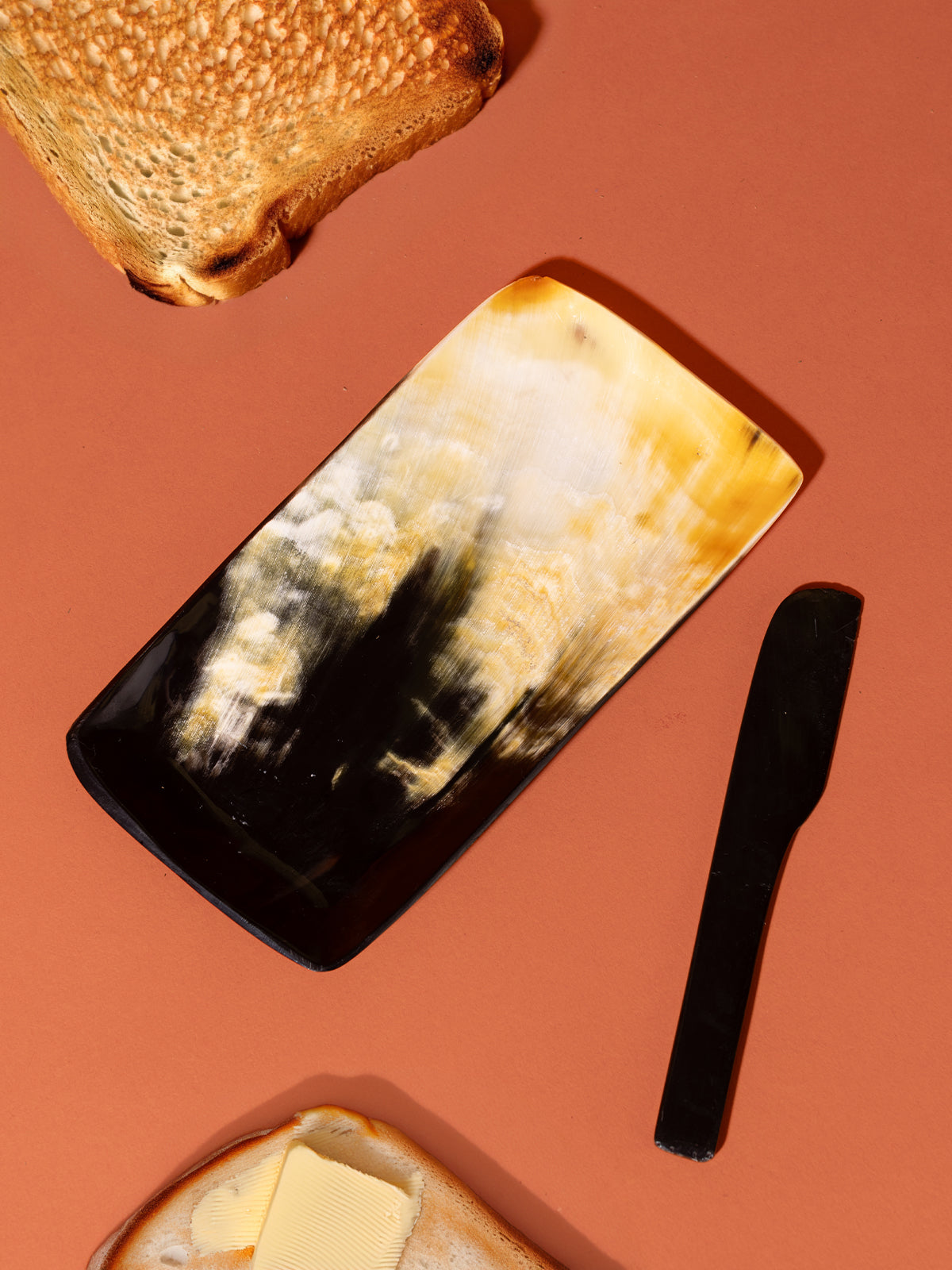 Butter tray and knife on orange background with toast and butter along the edges of the image. 