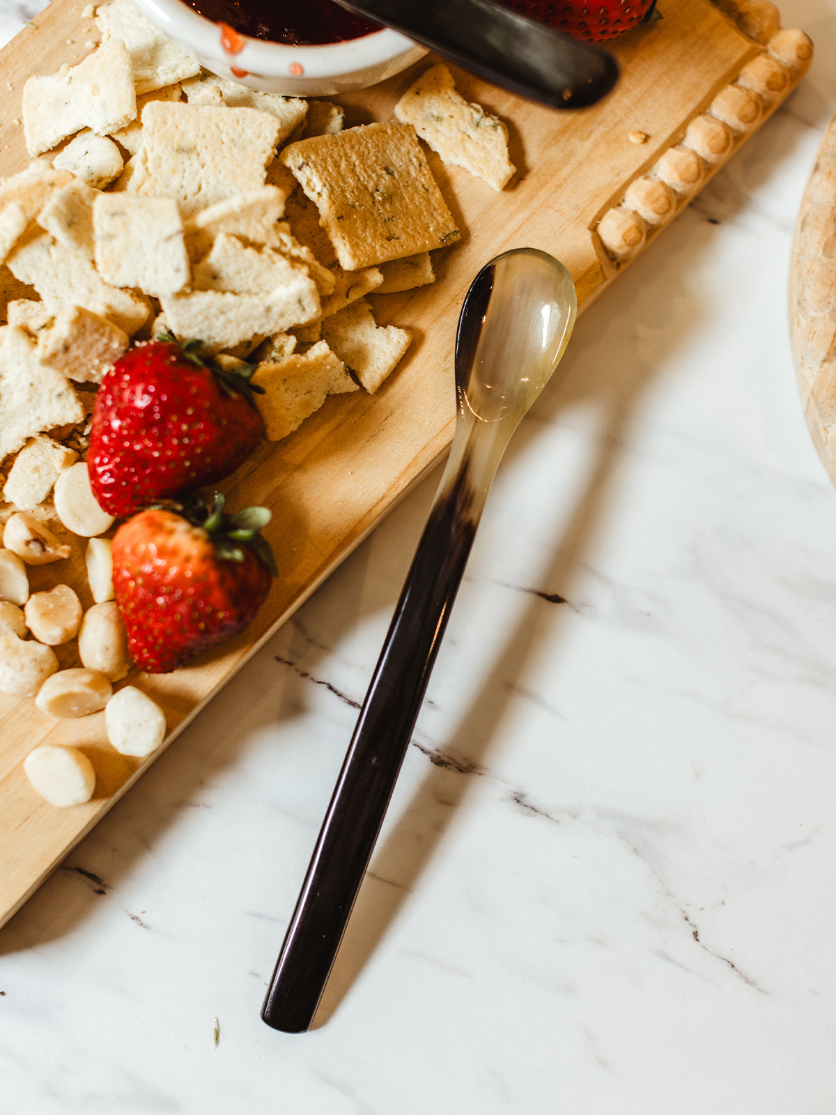 Long horn spoon with charcuterie board with crackers and berries. All object ate a white kitchen counter. 