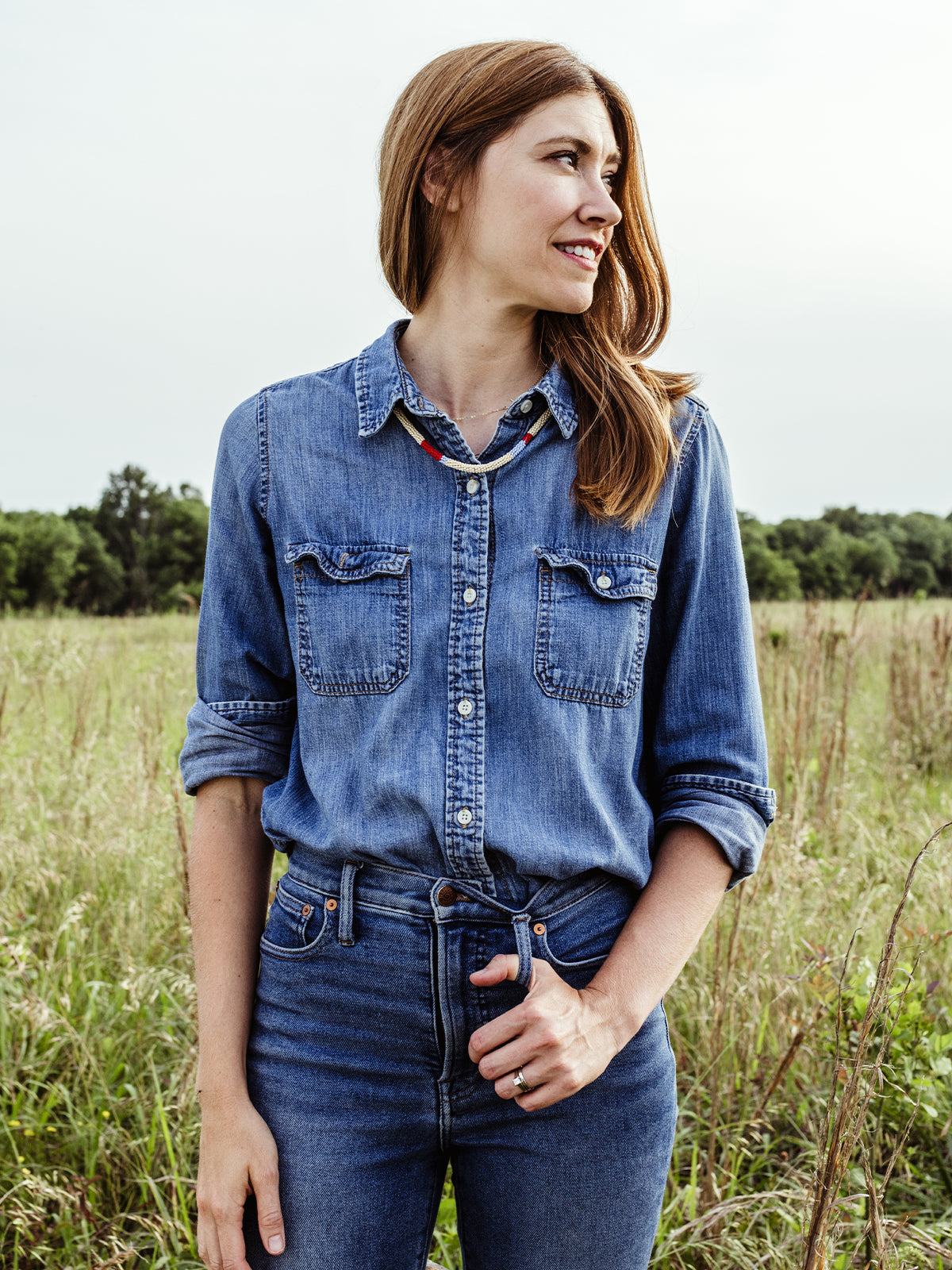 Female model with red hair wearing all denim wearing beaded Milot Necklace in outdoor setting. 