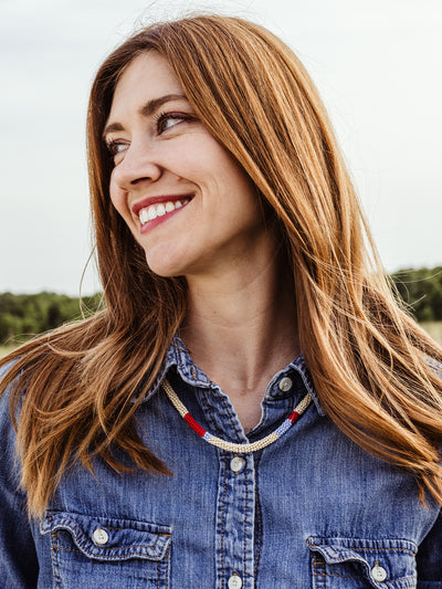 Portrait of female model with red hair wearing all denim wearing beaded Milot Necklace in outdoor setting. 