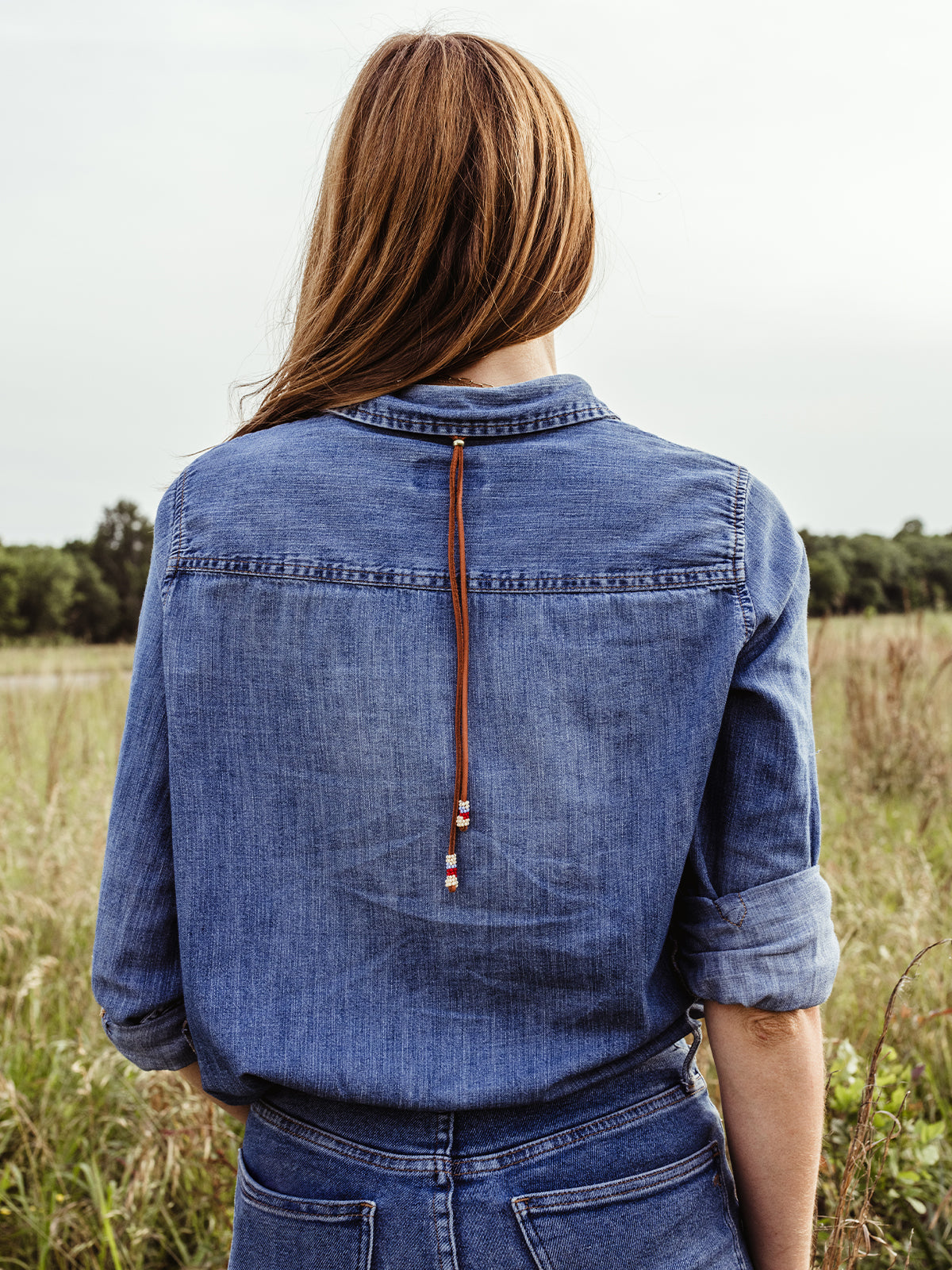 Female model wearing Milot Necklaced with back facing the camera to show adjustable long leather ties from the necklace. Ties extend to mid-back.