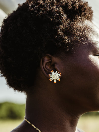 Close up of beaded sunburn earrings on female African model in outdoor setting. 