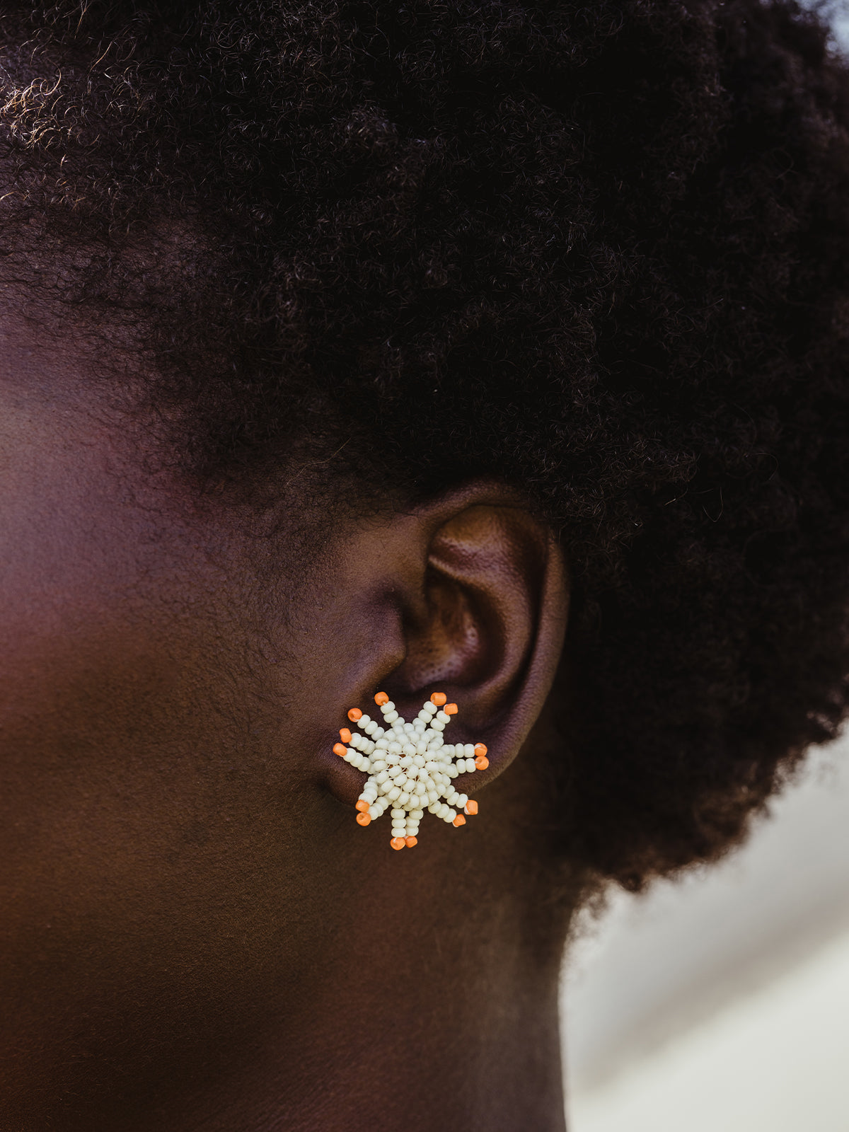 Close up of beaded sunburn earrings on female African model in outdoor setting. 