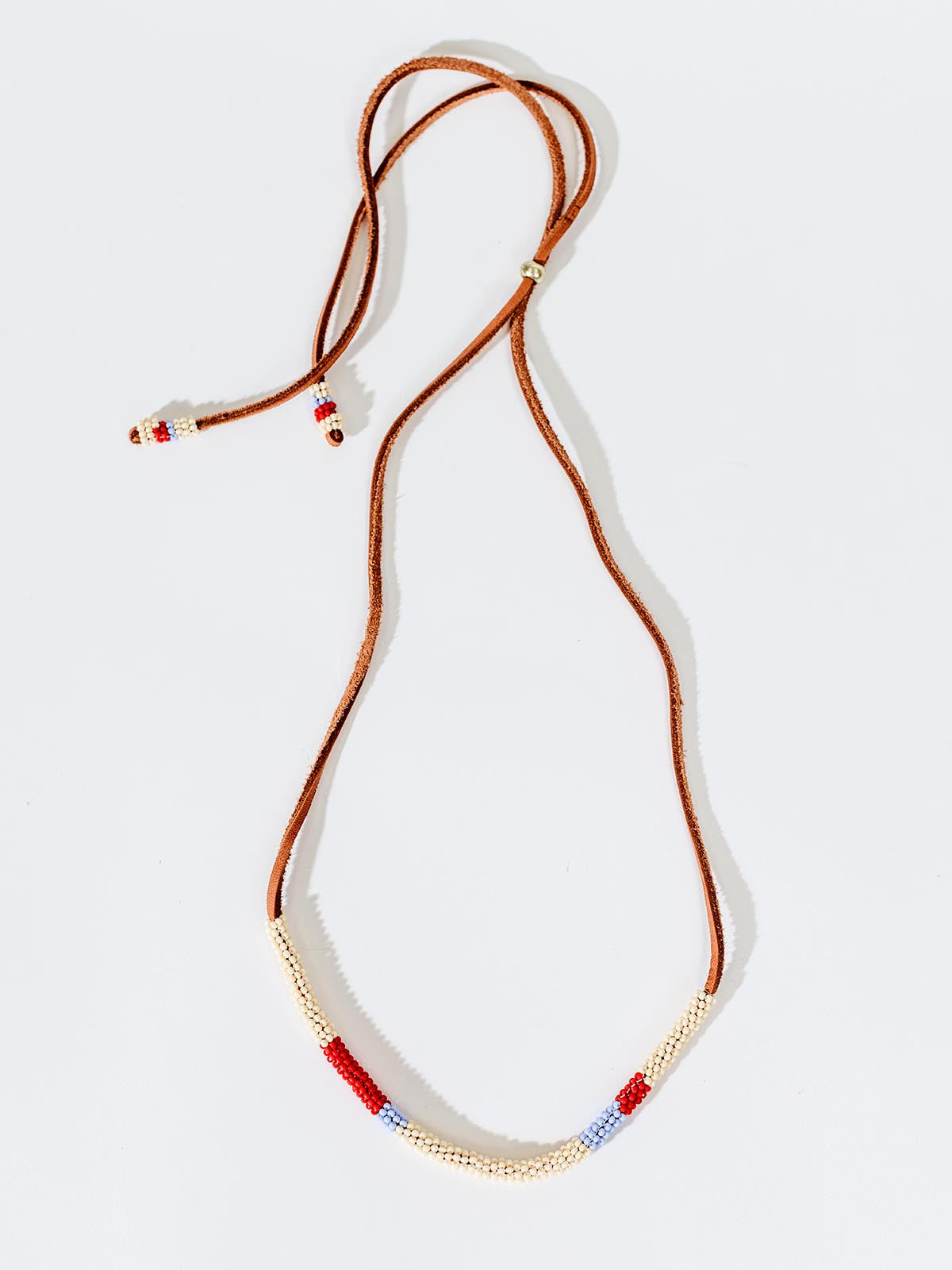 Milot necklace on white background. Necklace consists of leather strap and red, white, and blue, beaded.