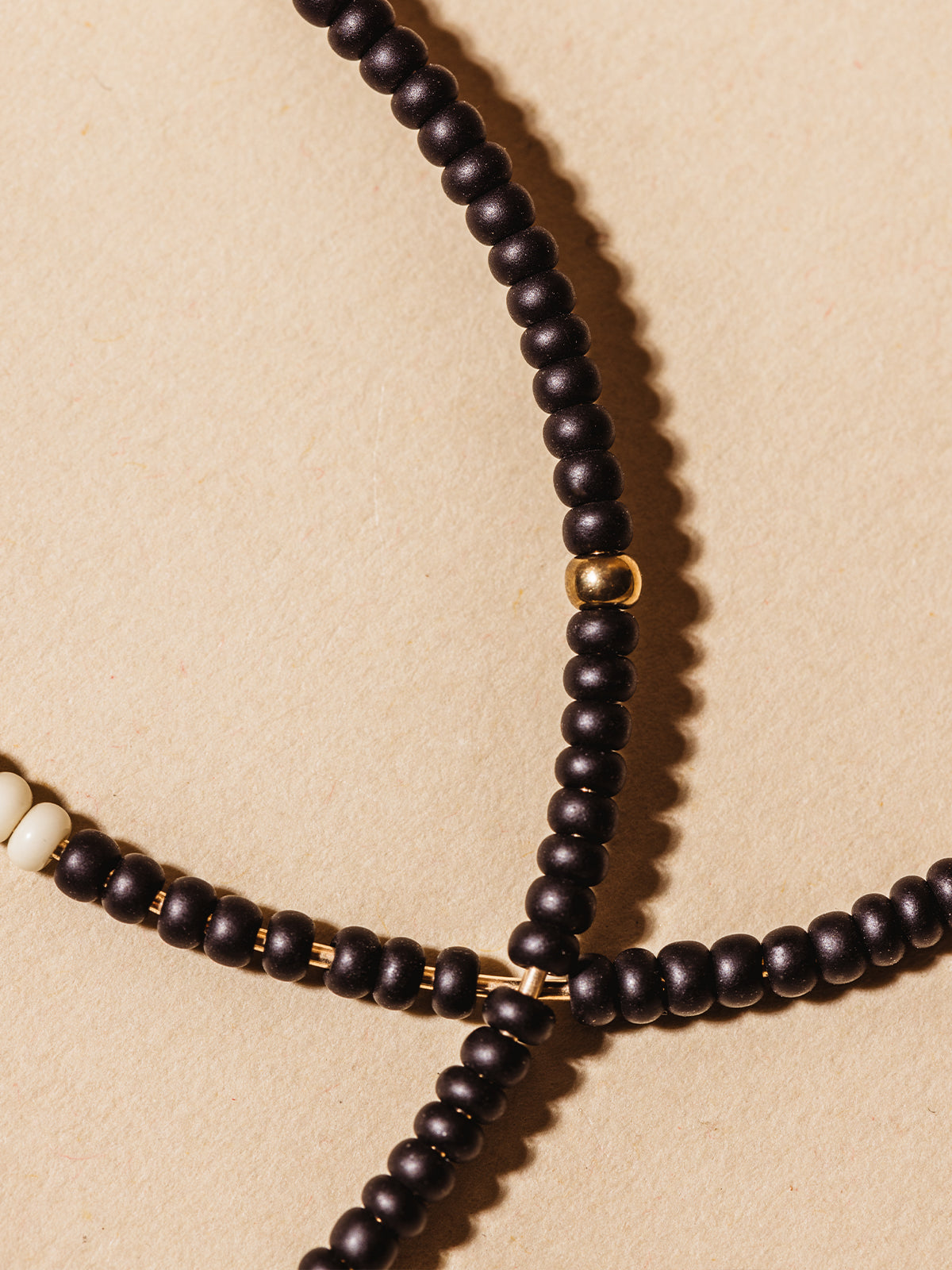 Close up of black, white, and gold beaded detail of the cafe hoops on a cream background. 