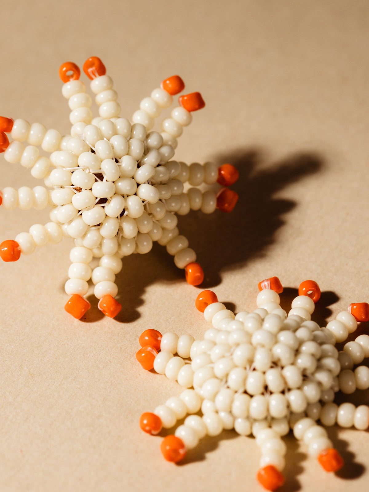 Orange and white beaded sunburst earrings on cream background. 