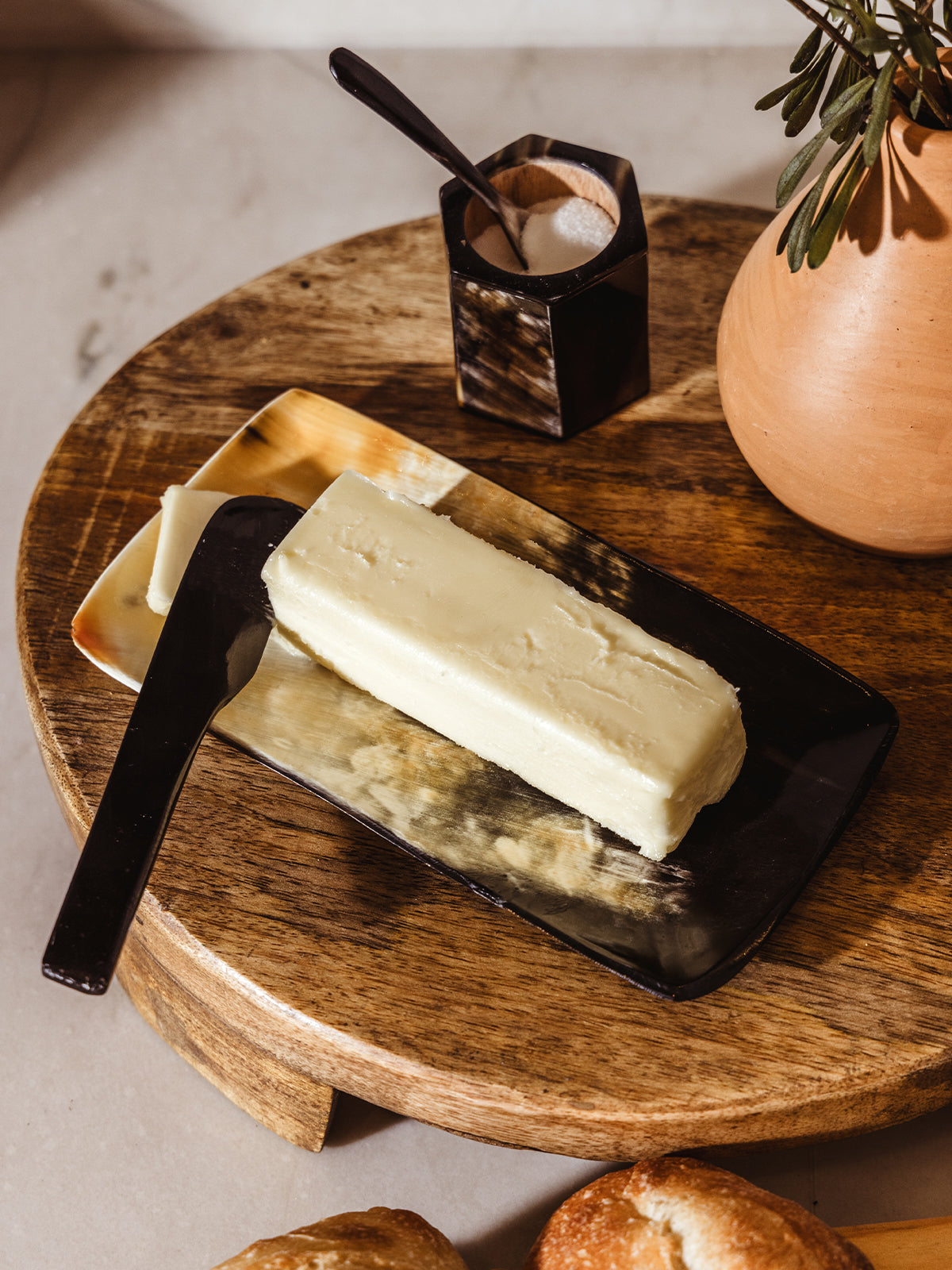 Horn butter tray and knife on wood riser on kitchen counter with bread rolls. 