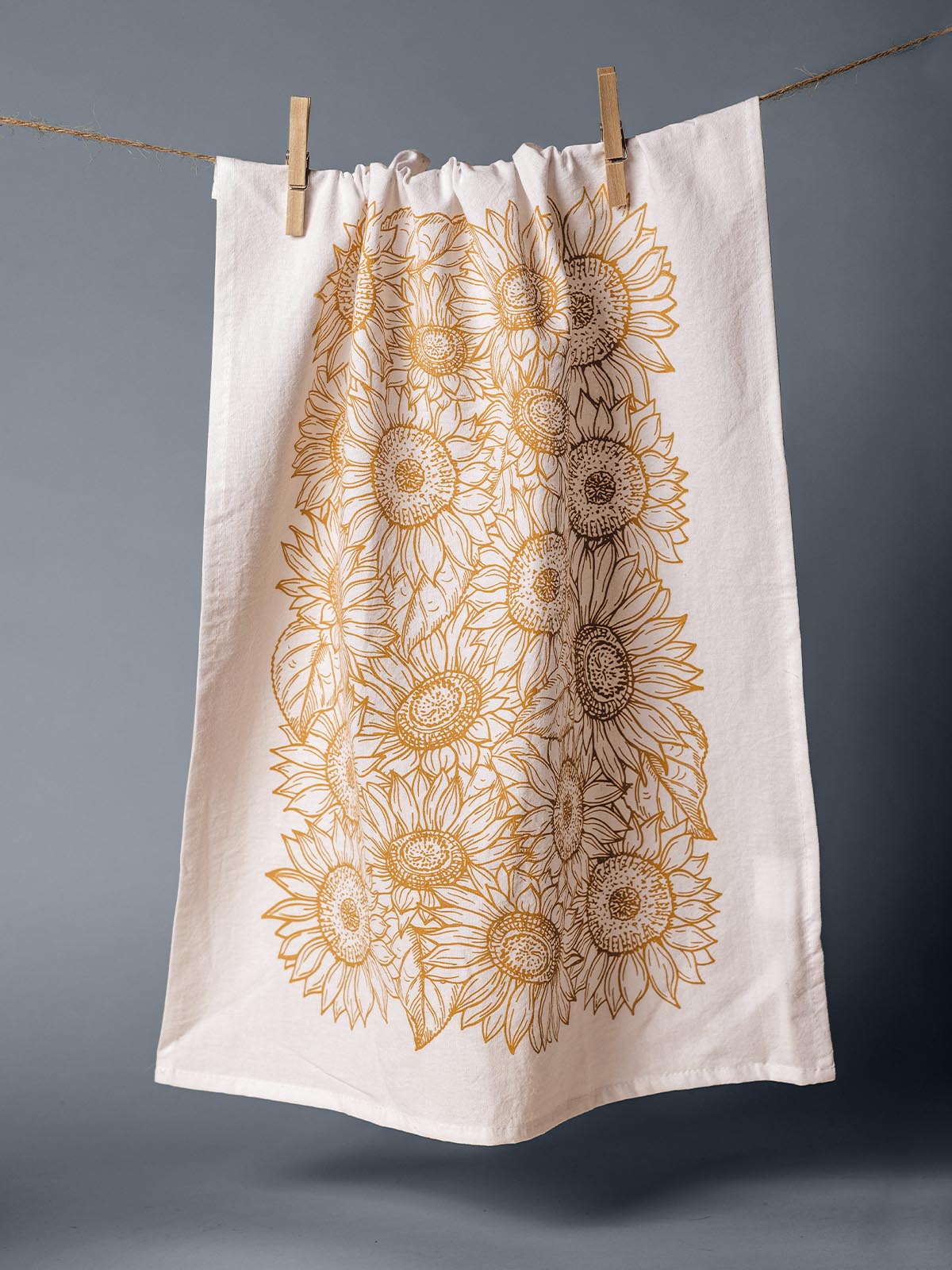 Hand-printed tea towel featuring an intricate sunflower design, hanging on a clothesline with clothespins, made from eco-friendly materials.