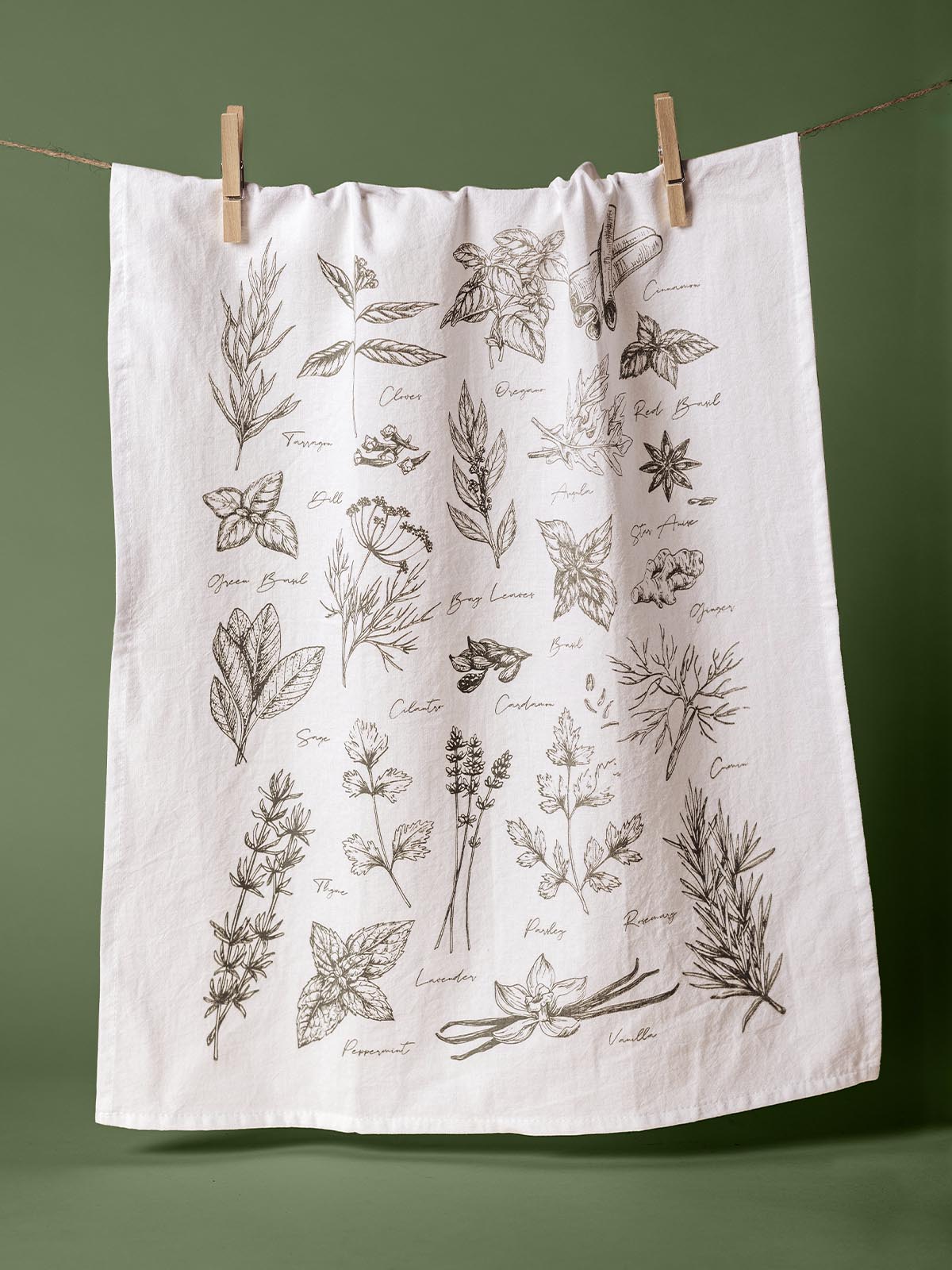 Hand-printed tea towel displaying a detailed botanical illustration of various herbs, hanging on a clothesline with clothespins, crafted from organic cotton.