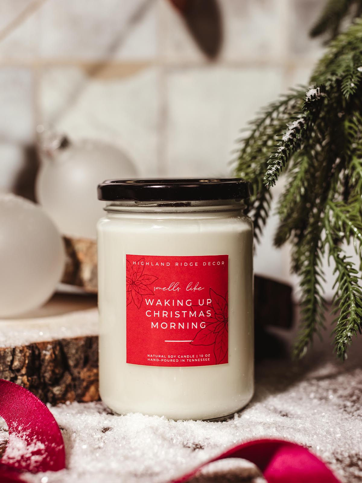 Hand-poured natural soy candle labeled 'Waking Up Christmas Morning' by Highland Ridge Decor, lit in a festive holiday scene with snow, greenery, and ornaments, perfect for holiday decor.