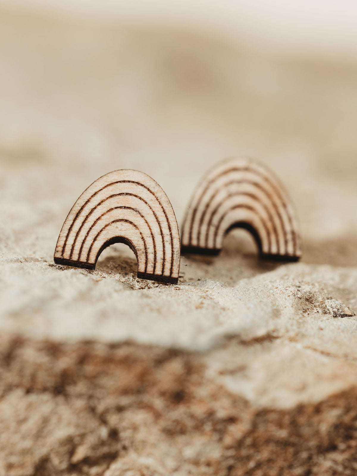 Close-up of handcrafted wooden rainbow earrings with a minimalist design, displayed on a natural stone surface.