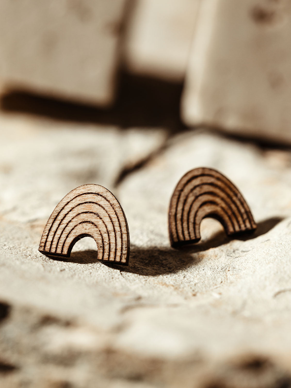 Pair of wooden rainbow-shaped earrings with engraved lines, placed on a textured natural background.