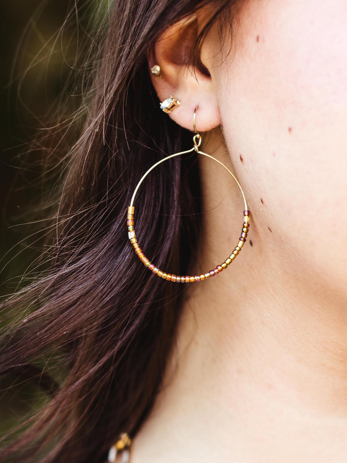 Detailed close-up of a handcrafted hoop earring with brown and gold beads worn by a woman, highlighting the delicate design.