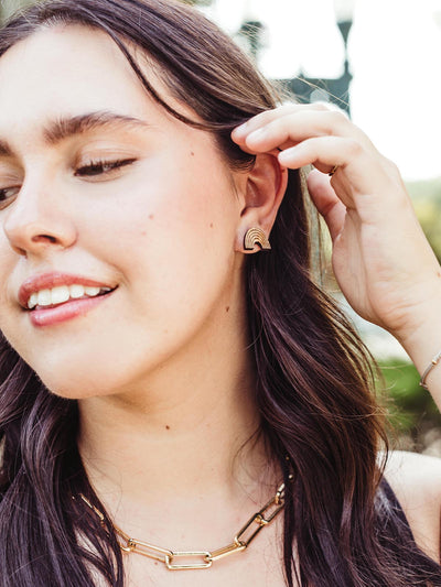 Woman wearing handcrafted wooden rainbow earrings with a minimalist design, paired with a gold chain necklace, photographed outdoors.