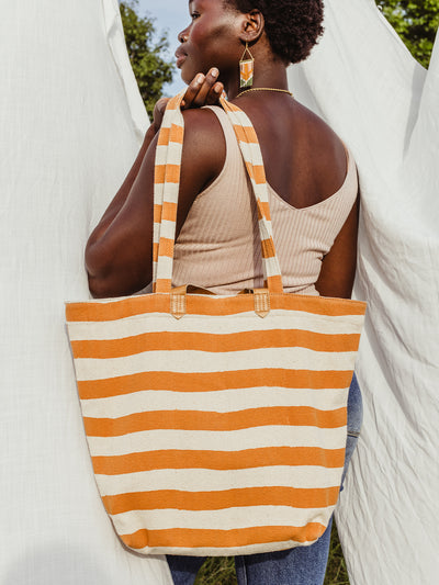 African female model in-front of white sheet holding canvas striped tote over her shoulder.