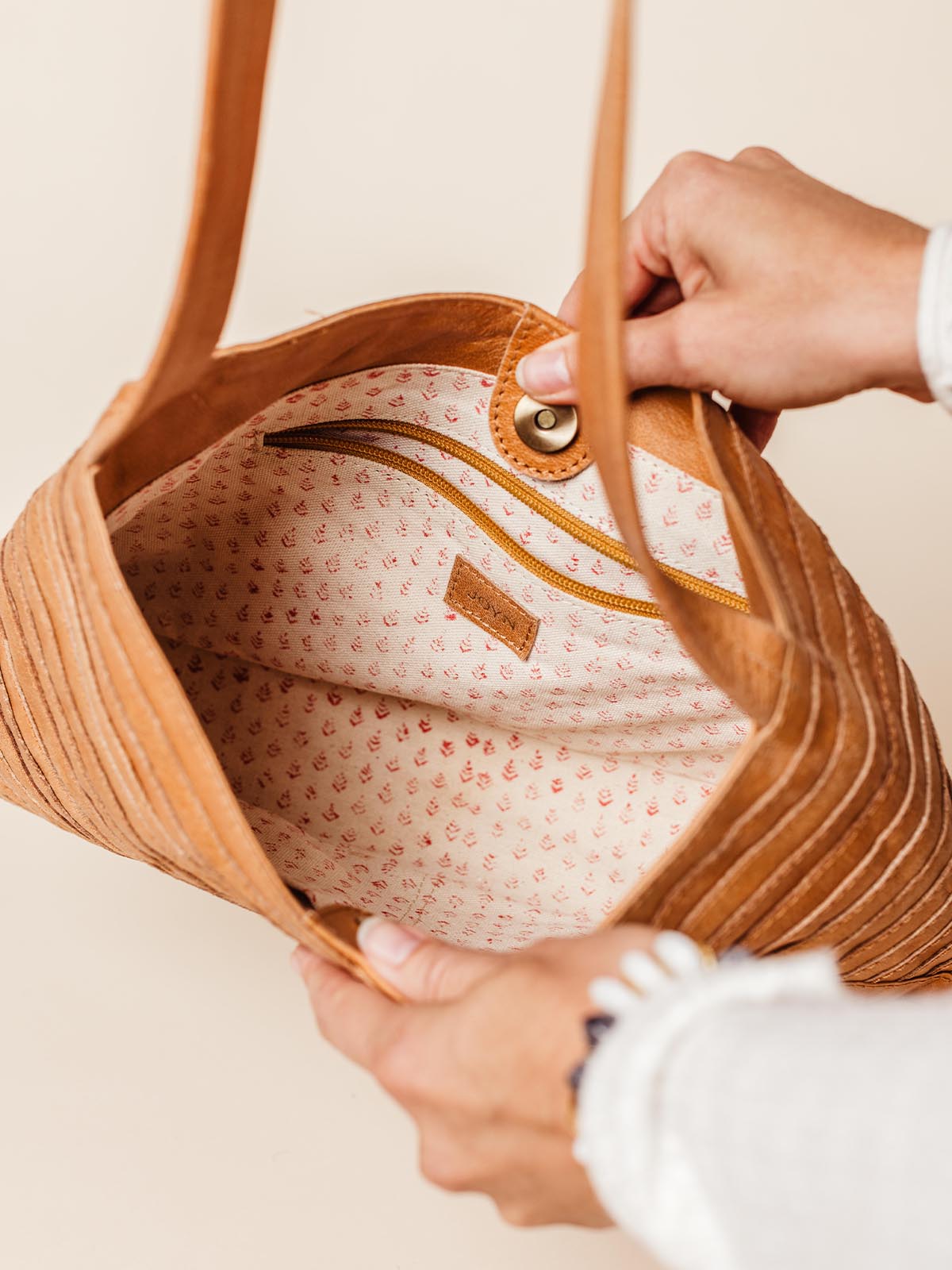 Close-up of the Crisscross Leather Handbag's spacious interior, featuring a patterned fabric lining, inner zipper pocket, and snap closure, handcrafted with sustainable materials, available at Joffa.