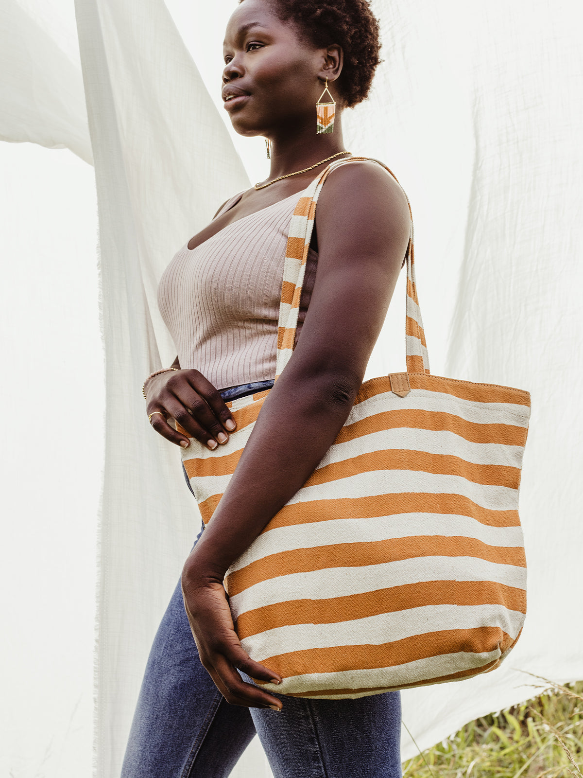 Female model in an outdoor setting  holding orange and cream striped canvas tote. 