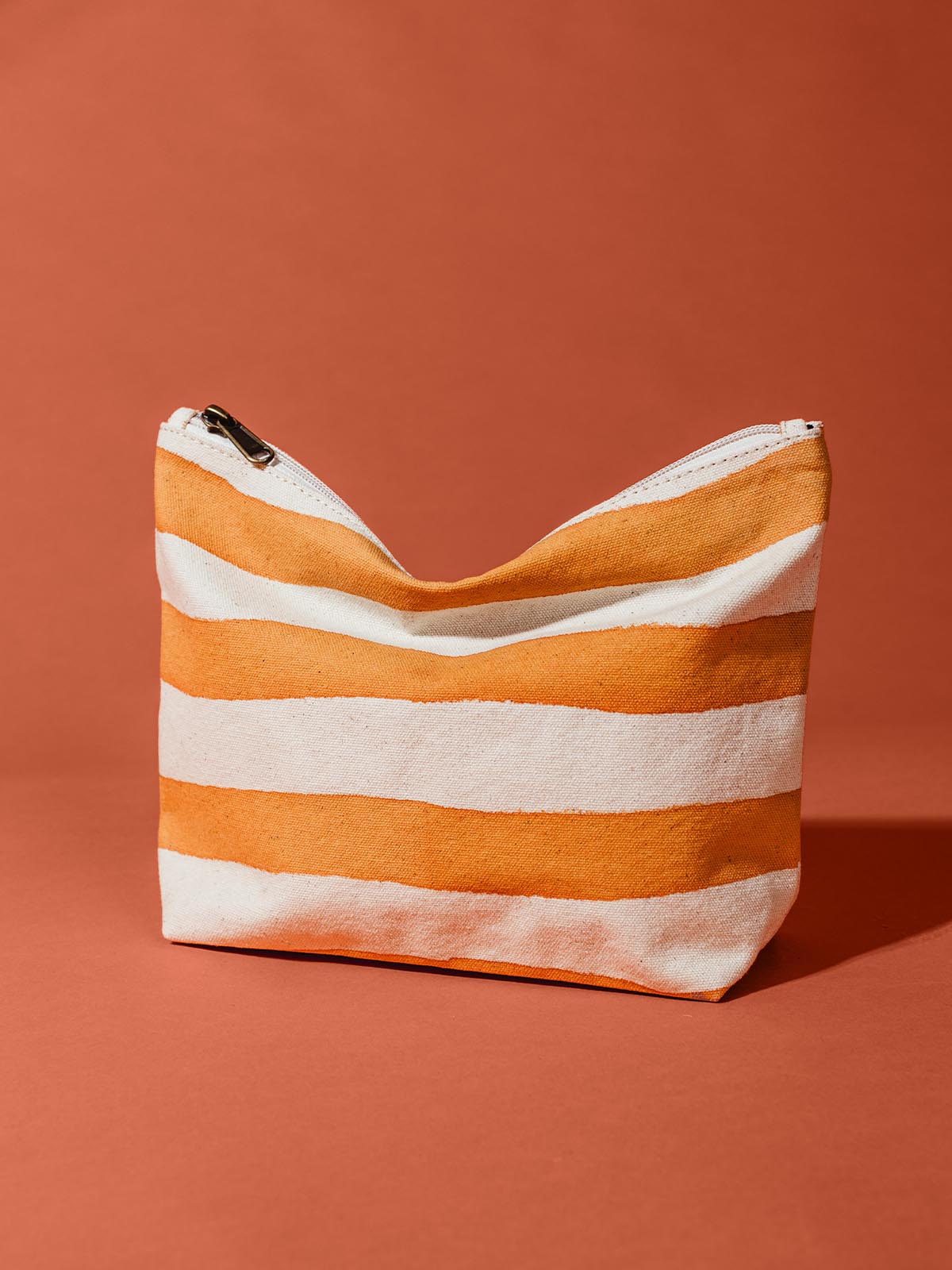 Orange and white striped waterproof pouch on rustic orange background.