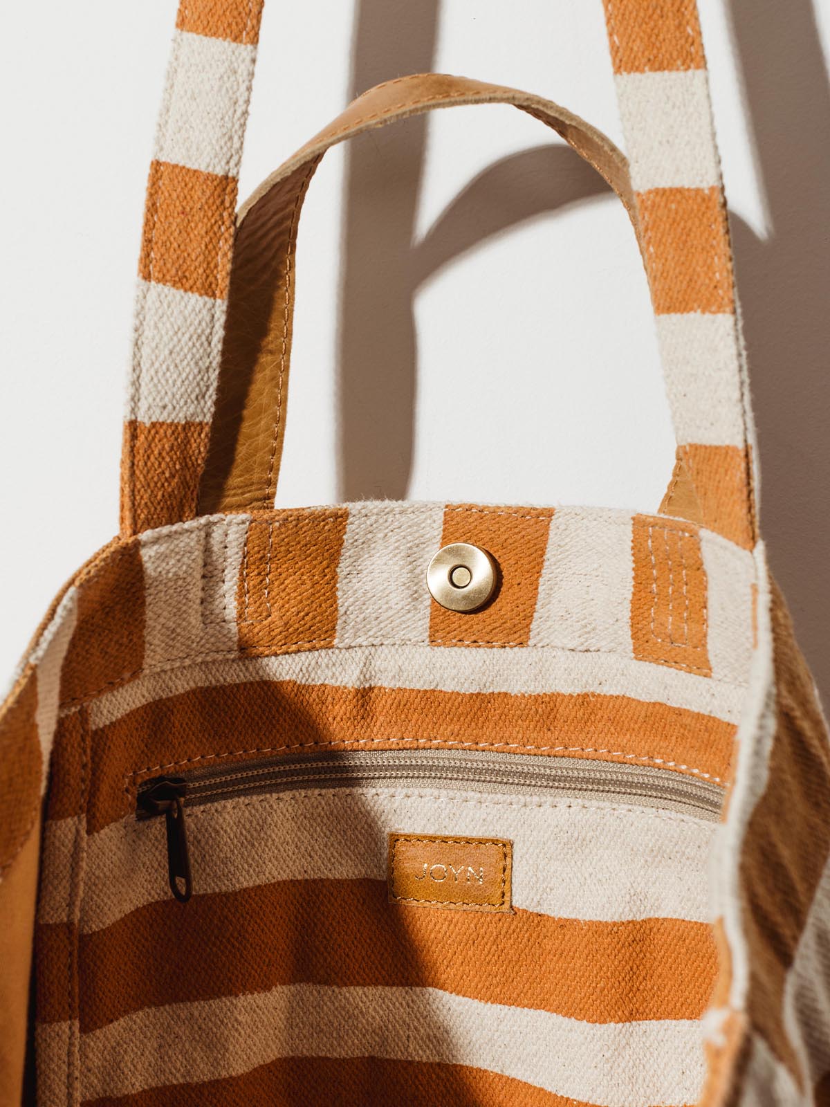 Inside zipper pocket on carryall canvas tote with cream and orange stripes on white wall hanging. 