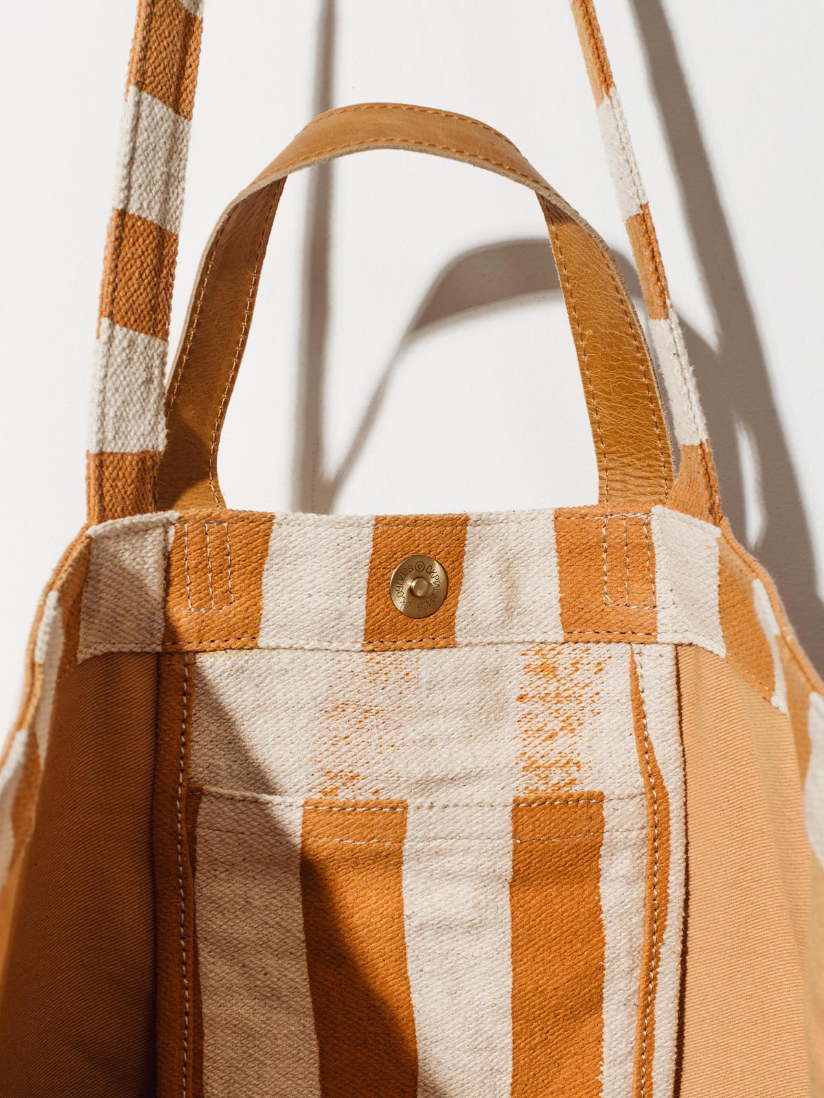 Inside slip pocket on carryall canvas tote with cream and orange stripes on white wall hanging. 