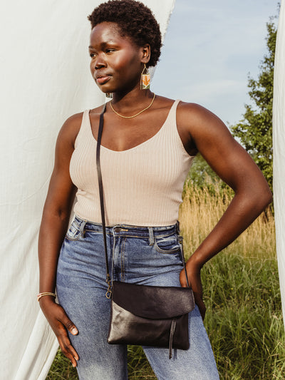 African female model in nature scene with black leather crossbody clutch over her outfit.