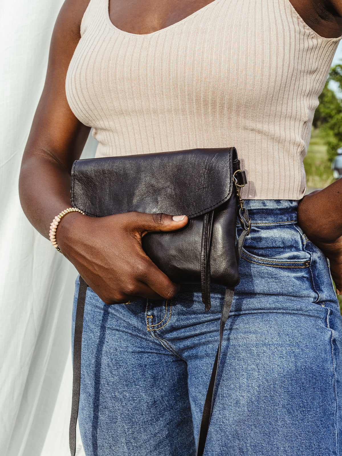 Close up of African female model in nature scene with black leather crossbody clutch over her outfit.