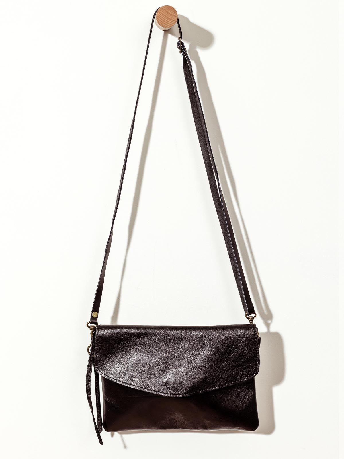 Black leather crossbody clutch on white wall.