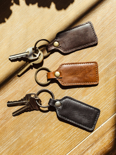 Back and blank side of leather keychains holding keys on wood table. 