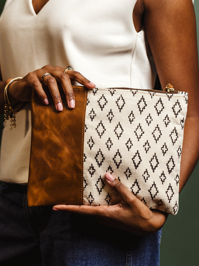 Detailed close-up of a woman holding a canvas and leather clutch bag with a geometric pattern. A versatile and stylish accessory for casual and formal occasions.